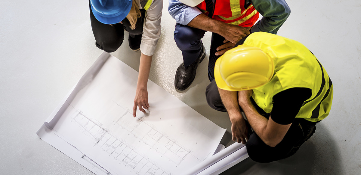 Two men in business attire and hard hats looking at a blueprint