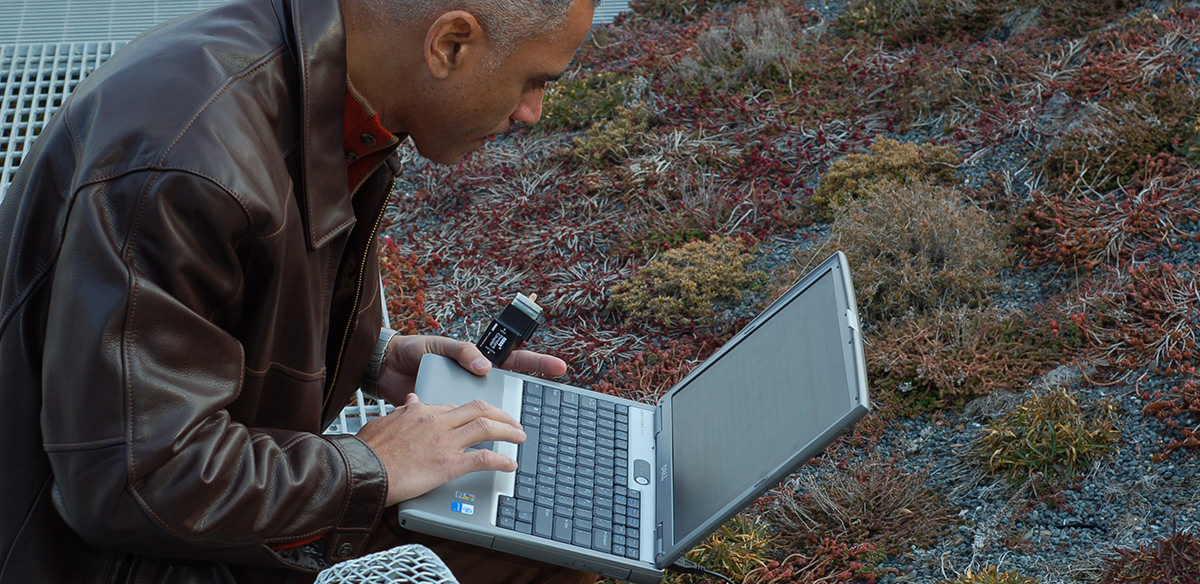 A man crouched on the ground holding a HOBO monitor and working on a laptop