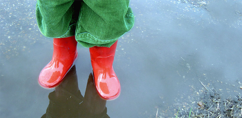 Child in rain boots standing in a puddle of water